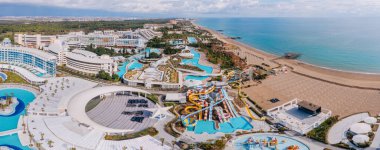 Serik, Türkiye - 28 Şubat 2025 - Havuz, su kaydırakları, modern mimari, palmiye ağaçları ve manzaralı kıyı manzaralı lüks bir sahil beldesi manzarası.