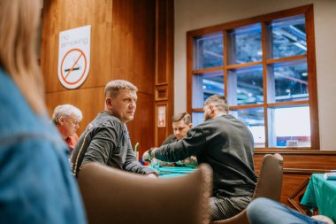 Belek, Türkiye - 22 Şubat 2025 - Bir grup erkek sosyal bir ortamda bir masada oturuyor, bir oyuna dahil oluyorlar. Ön planda bir adam odaklanmış bir ifadeyle yan tarafa bakıyor..