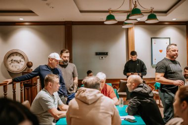 Belek, Türkiye - 22 Şubat 2025 - Bir grup erkek bir bardaki poker masasının etrafında toplandı, bazıları kağıt oynarken diğerleri gözlemledi. Ortam sıcak ve sosyal bir atmosfere sahip..