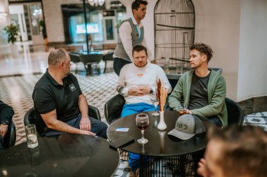 Belek, Türkiye - 22 Şubat 2025 - Bir grup adam şık bir salonda oturmuş, masada içkilerle sohbet ederken, bir garson modern bir ortamda yakınlarda duruyor..