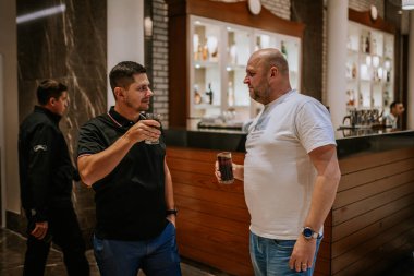 Belek, Türkiye - 22 Şubat 2025 - İki erkek şık bir barda içki içip sohbet ediyorlar, bardaklarını tutuyorlar ve rahat bir atmosferde öylesine tartışıyorlar..