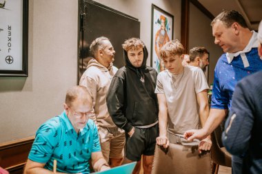 Belek, Türkiye - 22 Şubat 2025 - Bir grup adam bir dizüstü bilgisayarın etrafında toplanarak bir şeyi dikkatle tartıştılar. Bazıları ayakta durur, diğerleri oturur, ekrana odaklanır.