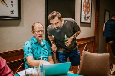 Belek, Türkiye - 22 Şubat 2025 - İki adam dizüstü bilgisayara bakarken bir tartışma içine girdi. Biri oturup açıklarken, diğeri bira şişesini tutuyor..