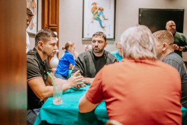 Belek, Türkiye - 22 Şubat 2025 - Bir grup adam yeşil keçeli bir masada ciddi bir kart oyunu oynadılar, stratejilerini tartıştılar. Diğerleri arka planda gözlem yapıyor..