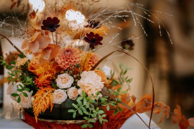 Koknese, Letonya - 26 Eylül 2023 - Turuncu ve beyaz güller, kurumuş yapraklar ve yeşillikler ile güzel bir çiçek düzenlemesi, zarif ve ılık bir sonbahar esinlenilmiş bir süs oluşturur..