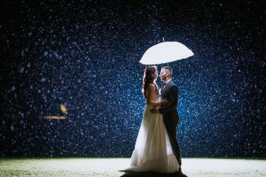 Koknese, Letonya - 26 Eylül 2023 - Romantik bir çift yağmurda parlayan bir şemsiyenin altında durur, birbirlerine bakarlar, sihirli arka ışıklandırmayla aydınlanırlar