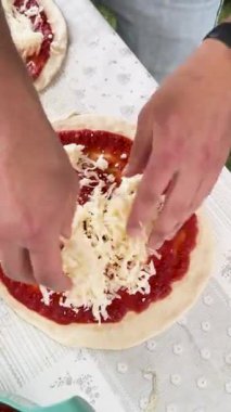 Bir insan taze hamurun üzerine rendelenmiş peynir dökerek ev yapımı pizza hazırlar..