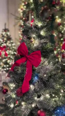 Süslü bir Noel ağacına yakın çekim kırmızı süslemeler, büyük kırmızı bir fiyonk ve parıldayan ışıklar, neşeli ve rahat bir tatil atmosferi yaratıyor..