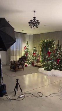 Valmiera, Letonya - 8 Aralık 2023 - Güzel dekore edilmiş Noel temalı bir fotoğraf stüdyosu içinde şenlik ağaçları, klasik bir sandalye, profesyonel ışıklandırma ve bir tripod bulunan.