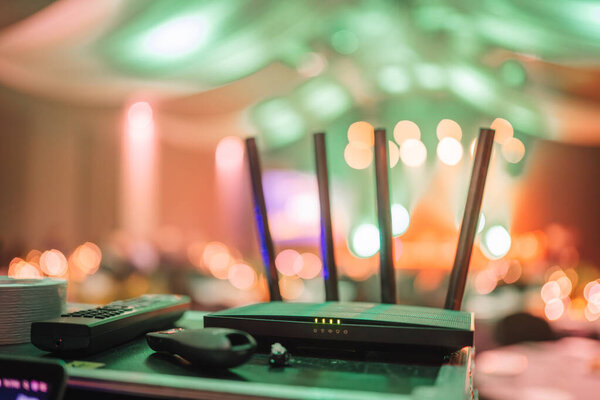 Валмиера, Латвия 29 ноября 2024 года - Wi-Fi-роутер с гаджетами в слабо освещенном месте проведения мероприятий, на заднем плане - боке и зеленая подсветка.