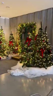 Çok güzel dekore edilmiş bir Noel sahnesi. Birden fazla parlak ağaç, kırmızı fiyonk, süsler, çelenkler ve hoş bir iç mekan dekorasyonu..