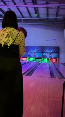 Riga, Letonya - 21 Kasım 2023 - Bir kadın neon ışıklı bovling salonunda topu yuvarlıyor eğlenceli ve hareketli bir gecede lobutlara doğru..