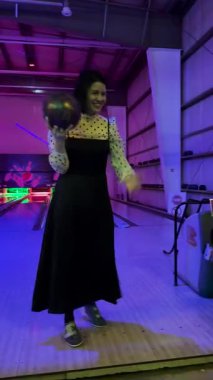 Bir kadın neon ışıklı bir bovling salonunda topu yuvarlıyor, lobutlara doğru yuvarlıyor eğlenceli ve hareketli bir gecede.