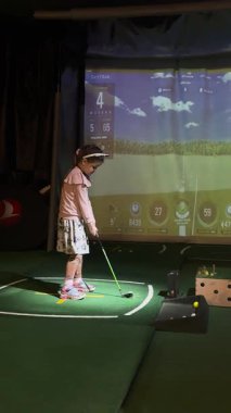 Bir golf koçu, genç bir kıza kapalı bir golf simülatöründe vuruşunu mükemmelleştirmesi için yardım eder. Yüksek teknolojili bir öğrenim ortamında elle eğitim sağlar..