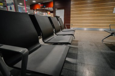 Riga, Letonya - 11 Kasım 2022 - Modern iç tasarımı, parlak döşemeleri ve ahşap panel duvarları olan bir havaalanı bekleme alanında boş siyah sandalyeler.