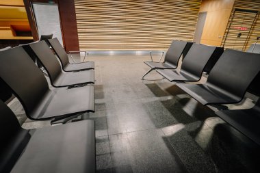 Riga, Letonya - 11 Kasım 2022 - Minimalist tasarımlı, ahşap kaplamalı ve parlak döşemeli modern bir havaalanında boş siyah sandalyeler.