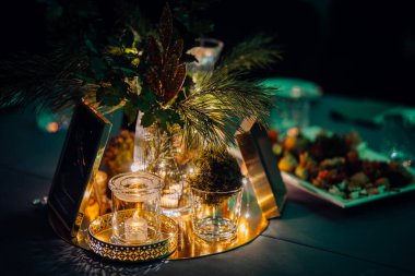 Çam dalları, mumlar ve altın süslemeleri olan zarif masa süsü resmi bir etkinlikte sıcak, şenlikli bir ortam yaratıyor..