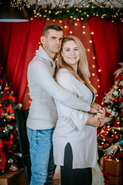 Sıcak Noel ışıklarının ve şenlikli dekorun önünde kucaklaşan gülümseyen çift, birlikte neşeli ve samimi bir tatil anı paylaşıyorlar..