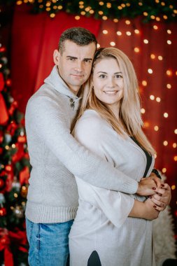 Sıcak Noel ışıklarının ve şenlikli dekorun önünde kucaklaşan gülümseyen çift, birlikte neşeli ve samimi bir tatil anı paylaşıyorlar..