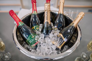 Valmiera, Letonya - 29 Kasım 2024 - Rgas etiketli şişeler buzla dolu büyük bir metal kasede soğutuluyor, şenlikli bir kutlamada veya etkinlikte servis edilmeye hazır hale getiriliyor.