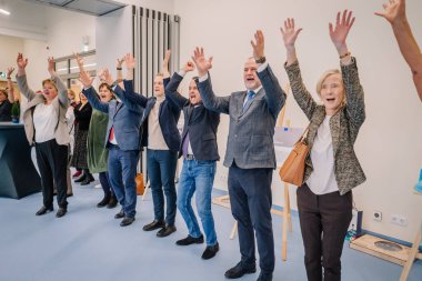 Valmiera, Letonya - 29 Kasım 2024 - Bir rehabilitasyon merkezinde düzenlenen etkinlik sırasında neşeli bir grup yetişkin ellerini kaldırarak, kapalı alanda birlik ve pozitif enerji gösterdiler..