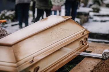 Valmiera, Letonya - 6 Ocak 2022 - Bir kış cenazesi sırasında tabutun yakın plan çekimleri ve bulanık arka planda yas tutanlar.