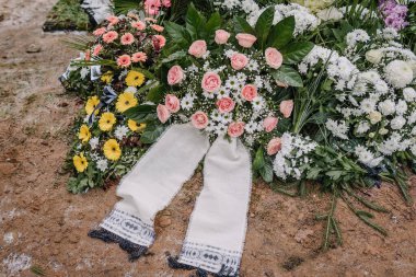 Valmiera, Letonya - 6 Ocak 2022 - Cenaze çiçeği düzenlemeleri pembe güller, papatyalar ve taze topraklarda geleneksel kumaş kurdeleler, renkli çiçeklerle çevrili.