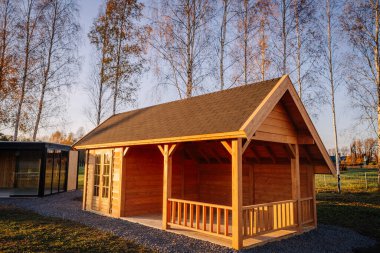 Konforlu ahşap kulübe, gable çatılı ve küçük verandalı, sıcak bir akşam güneşi altında, arka planda ağaçlarla birlikte huzurlu kırsal bir arazide yakalandı..