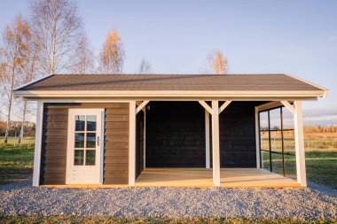 Sonbahar aylarında huzurlu bir kırsal alana kurulmuş beyaz bukle ve cam kenarlı modern ahşap kulübe, sıcak güneş ışığıyla aydınlatılıyor..