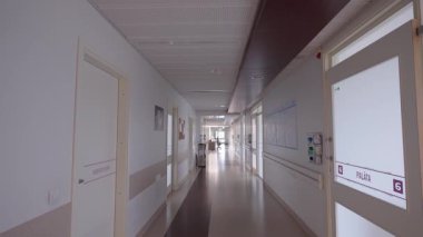 Valmiera, Letonya - 24 Mart 2025 - Etiketli hasta ve servis odası kapıları, duvar takvimi çizelgeleri ve uzak hemşire istasyonu olan parlak hastane koridoru.