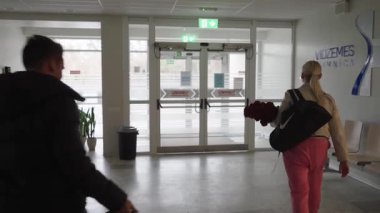 Valmiera, Letonya - 24 Mart 2025 - Bir çift, Vidzemes Hastanesi 'nin girişinde arkadan görülen çantalar, çiçekler ve bebek arabası koltuklarıyla hastaneden ayrıldı.