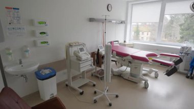 Valmiera, Letonya - 24 Mart 2025 - Kırmızı doğum odası, tıbbi ekipmanlar, monitörler, lavabo ve doğal ışık sağlayan büyük pencereli modern hastane doğum odası.
