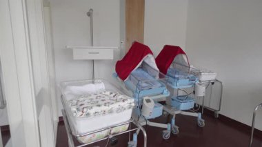 Valmiera, Letonya - 24 Mart 2025 - Üç bebek beşiği bulunan hastane yeni doğan odası, ikisi gölgeyle kaplı, battaniyeler, monitörler ve mobil tıbbi destek ekipmanlarıyla donatılmış.