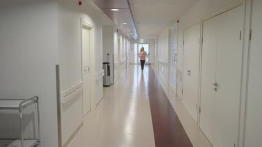 Valmiera, Letonya - 24 Mart 2025 - Bir kadın elinde yeni doğmuş bir bebekle hastane koridorunda yürüyor, etrafı temiz beyaz duvarlarla, kapılarla ve sakin bir ortamda hafif aydınlatmayla çevrili..