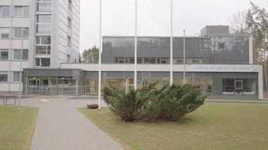 Valmiera, Letonya - 24 Mart 2025 - Geniş pencereli, bayrak direkli, manzaralı yürüyüş yolu ve etrafındaki çam ağaçlarıyla çevrili modern bir rehabilitasyon merkezi.