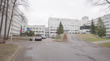 Valmiera, Letonya - 24 Mart 2025 - Birçok beyaz binası, otoparkı, servis minibüsü ve bulutlu bir günde ana girişe çıkan merdiveni olan büyük bir hastane kompleksi.