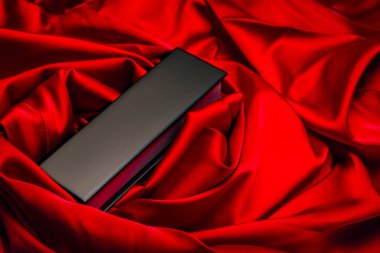 Zarif kıvrımlı, kırmızı saten kumaşa yerleştirilmiş parlak siyah dikdörtgen kutu ürün veya hediye sunumları için ideal lüks ve dramatik bir sahne oluşturuyor..
