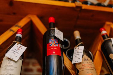 Riga, Letonya - 27 Mart 2025 - Ahşap şarap rafında el yazısıyla etiketlenmiş şarap şişelerinin yakın çekimi, sıcak bir mahzende İtalyan kırmızı şarapları sergileniyor.