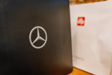 Riga, Letonya - 27 Mart 2025 - Siyah bir Mercedes-Benz hediye çantasının yakınında, ahşap bir yüzey üzerinde, iyi aydınlatılmış bir iç mekanda, beyaz bir Illy marka çantanın yanında..