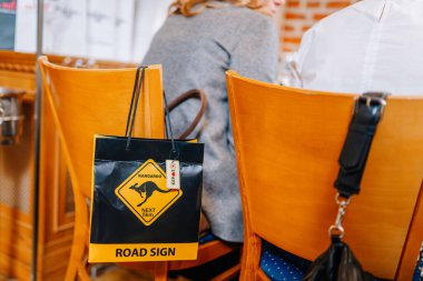 Riga, Letonya - 27 Mart 2025 - Kanguru yol tabelası dizaynlı renkli bir hediye çantası, kapalı bir ortamda ahşap bir sandalyede, çantaların yanında ve oturanların yanında asılı duruyor..