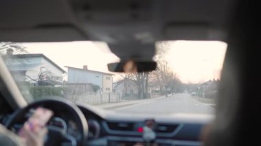 Valmiera, Letonya - 2 Mart 2025 - Gün batımında sakin bir banliyö mahallesinden geçerken, sürücü ve bir yolcunun hafif bir odak noktasında görüldüğü bir arabanın içine bakın.