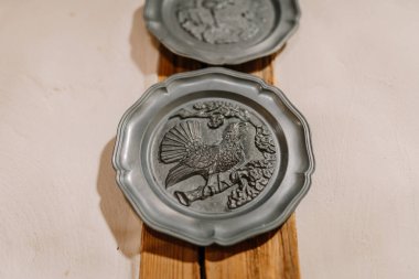 Madona, Letonya - 15 Şubat 2025 - Kabartmalı kuş ve ağaç desenli dekoratif metal plaka, sade bir duvara monte edilmiştir..