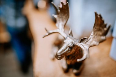 Madona, Letonya - 15 Şubat 2025 - Büyük boynuzlu bronz geyik heykelciği ahşap bir yüzeye yerleştirilmiş, sanatsal odaklanma için sığ bir alan derinliği olan kırsal bir iç mekânda yakalandı.