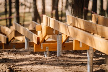 Kumlu, ağaçlık bir ortamda orman yolu inşaatı sırasında metal zemine monte edilmiş ahşap merdiven korkuluklarının yakın görüntüsü..