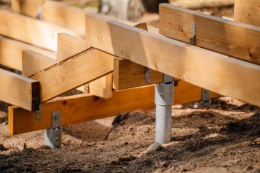 Orman bölgesinde inşaat halindeki ahşap merdivenlere yakın çekim. Metal zemine monte edilmiş destek kirişleri kumlu toprakta emniyette..