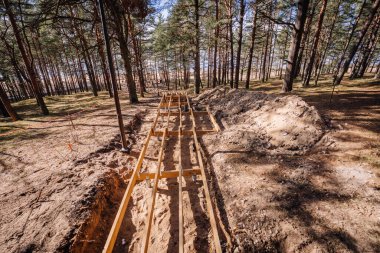 Tahta merdiven iskeleti kumlu bir orman tepesinde, ağaçlar ve dikkat bantlarıyla çevrili, uzaktaki sahile doğru gidiyor..