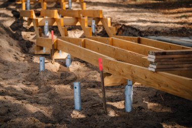Metal vida yığınları ve destek kirişleri ile kumlu bir orman bölgesinde yapım aşamasında olan ahşap kaldırım, açık hava yolu inşaatının ilerlemesini gösteriyor..
