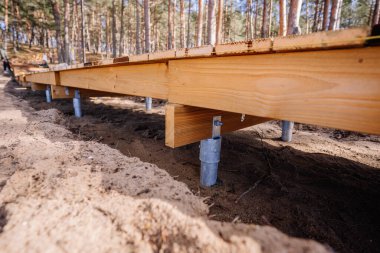Tahta kaldırım yapısı galvanize metal vidalar tarafından destekleniyor, kumlu orman arazisi üzerine inşa edilmiş, açık hava inşaat projesinin bir parçası..