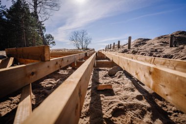 Açık mavi gökyüzünün altında kumlu bir sahil bölgesinde yapım aşamasındaki ahşap bir sahil yolunun alçak açılı görüntüsü..