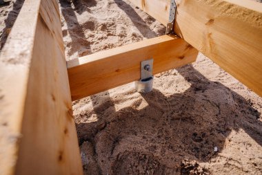 Açık hava inşaat projesinin bir parçası olan kumlu toprağa demirlenmiş ahşap tahta kaldırım destek iskeletinin yakın çekimi..